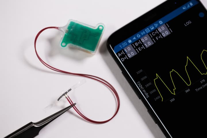 A set of tweezers holds one of the sensors (bottom), which is hard-wired to an implanted base station (green)